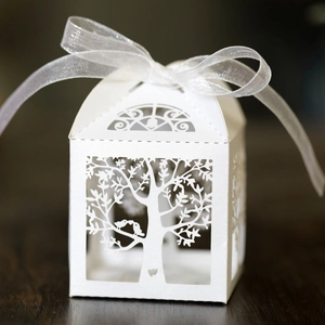 Detailed laser-cut tree and lovebird design on a white paper candy box with ribbon