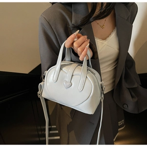 Detail of light blue patent leather bag with heart motif and adjustable strap worn by model