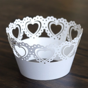 Detail of white laser-cut cupcake wrappers with heart pattern on dark wood background