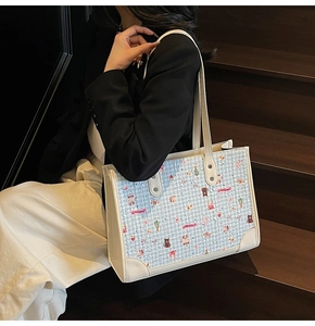 Détail du sac cabas tissé bleu à motifs de dessins animés porté par un mannequin en blazer