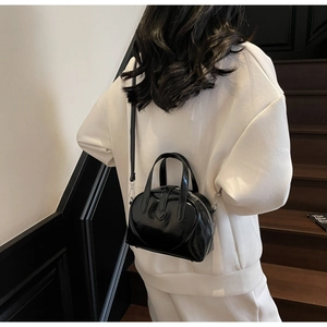 Detail of a shiny black leather bowling bag with heart motif shown on a model