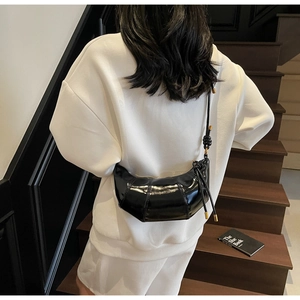 Detail shot of a black glossy crescent croissant bag with stitched texture on a white outfit