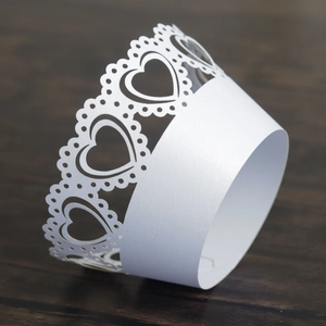 Intricate laser-cut heart pattern on white pearlescent cupcake wrappers for weddings