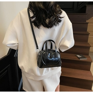 Close-up of black glossy heart-shaped handbag with adjustable strap on a white hoodie