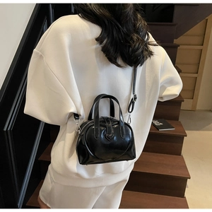 Detail of a black glossy heart-shaped bag shown in a stylish outdoor setting