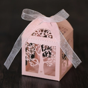 Detailed laser-cut tree and bird pattern on pink paper candy gift box with white ribbon