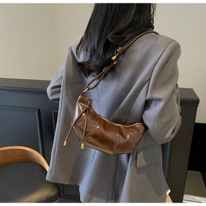 Detail shot of a dark brown croissant shoulder bag featuring pleated leather and metallic accents