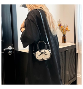 Dettaglio mini borsa a tracolla con fiocchi neri e ciondolo a cuore su tessuto bianco