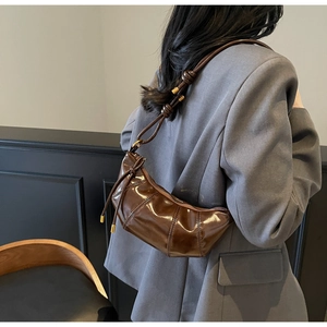 Detail of coffee brown glossy faux leather crescent bag with stylish knotted shoulder strap