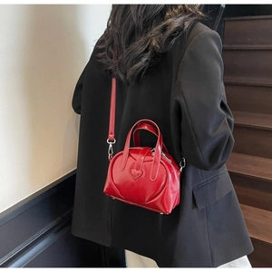 Chic red heart-shaped shoulder bag in glossy leather worn by a model in black blazer