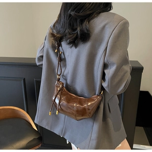 Detail of dark brown leather croissant bag with knotted strap and gold hardware accents