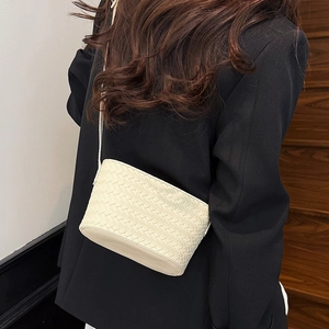 Detail of a cream woven crossbody bag shown on a model wearing a black blazer jacket