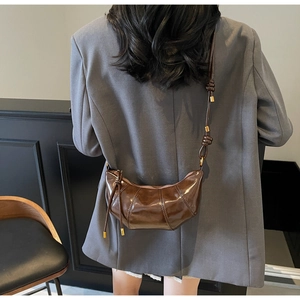 Detail view of brown glossy leather crossbody bag with pleated texture and knotted shoulder strap