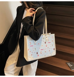 Détail du sac cabas en tweed bleu avec motifs de dessins animés et anses en cuir blanc