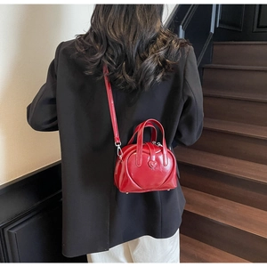 Detail of red heart-shaped patent leather crossbody bag on a model in a lifestyle setting