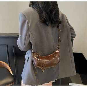 Detail of a dark brown glossy leather dumpling bag with knotted strap and gold hardware