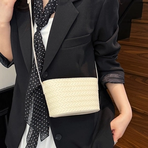 Detail view of cream woven crossbody bag on model with black suit and polka dot scarf