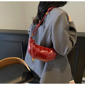 Detail of red glossy leather crescent bag with knotted shoulder strap worn by a model
