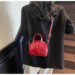 Detail of red heart-shaped leather bag featuring a silver metal D-ring and crossbody strap