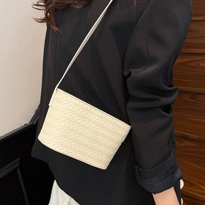 Close-up of minimalist cream woven leather crossbody bag shown on model with black blazer