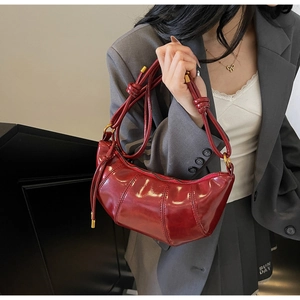 Detail of burgundy glossy half-moon bag with knot strap and golden metal hardware
