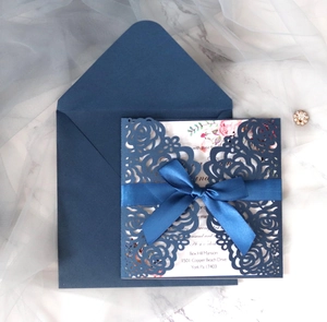 Detail of navy blue laser cut rose wedding invitation with silk bow on marble surface