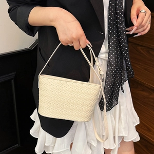 Detailed close-up of cream woven bucket bag texture with slim leather strap