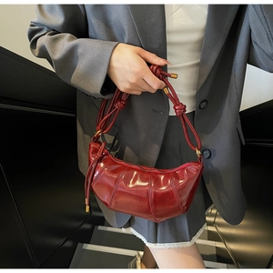 Detailed close-up of a burgundy patent leather dumpling bag with knotted strap and gold hardware