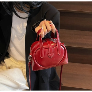 Detail of burgundy leather Boston bag featuring a stitched heart and adjustable strap