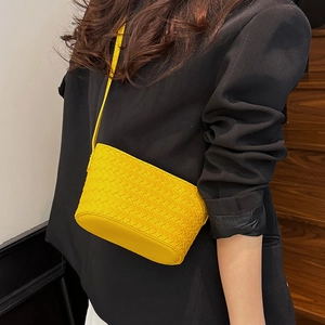 Close-up of a bright yellow woven bucket bag worn across a stylish black blazer