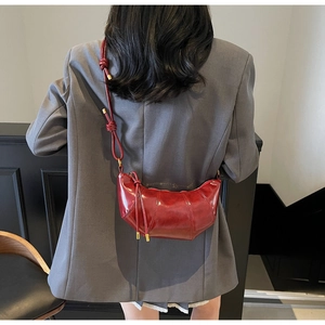 Detail of red-brown glossy croissant bag with knotted adjustable strap on model