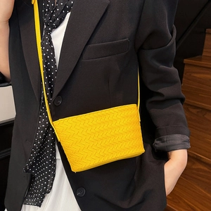 Close-up of bright yellow woven leather crossbody bag styled with a dark blazer