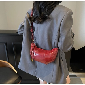 Deep red croissant bag in quilted glossy leather worn over a grey blazer on model