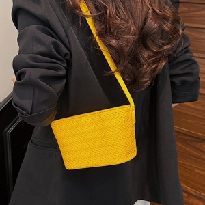 Detail of yellow woven crossbody bag highlighting the texture against a black suit