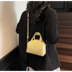 Pale yellow Boston bag with heart detail worn over the shoulder by a model in a black blazer