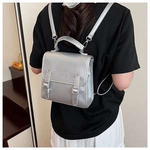 Silver metallic backpack with handle and embossed lettering worn by a model in a casual setting