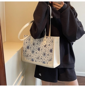 Gros plan d'un sac cabas crème avec motifs d'ours porté à l'épaule par un mannequin