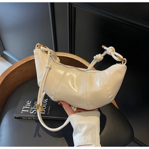Detail of creamy white patent leather hobo bag with quilted texture and knot strap