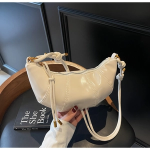 Detailed close-up of cream-white glossy croissant bag with elegant knotted shoulder strap