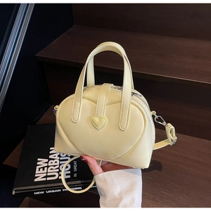 Detail of cream yellow underarm bag with embossed heart and silver metal hardware