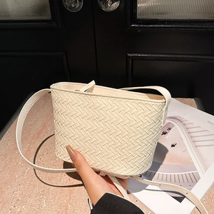 Detail of cream woven leather bucket bag with adjustable strap on marble surface