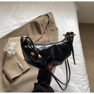 Detail of black pleated croissant bag with gold zipper and smooth leather texture