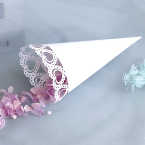 Detail of white laser-cut heart pattern wedding cone with purple dried flower petals