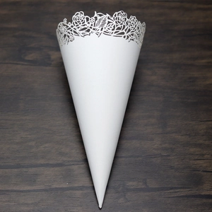 Detail of white laser-cut wedding petal cone with elegant rose patterns on wood background