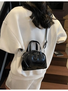 Glossy black heart-shaped boston bag with adjustable strap on a wooden staircase