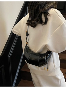 Modern black glossy patent leather crescent crossbody bag with unique knot shoulder strap