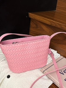 Pink woven leather shoulder bucket bag with adjustable strap on white fabric background