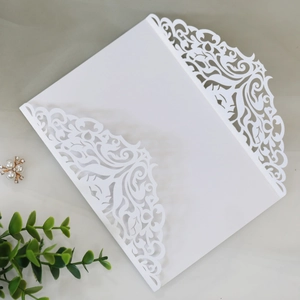 Λεπτομερές σχέδιο laser-cut σε λευκή κάρτα προσκλητηρίου γάμου με πέρλες και διακόσμηση