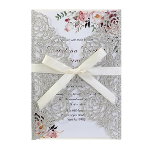 Macro detail of laser-cut glitter silver wedding invitation with cream ribbon bow