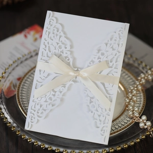 Close-up of laser cut hollow invitation cover with white satin ribbon and lace details
